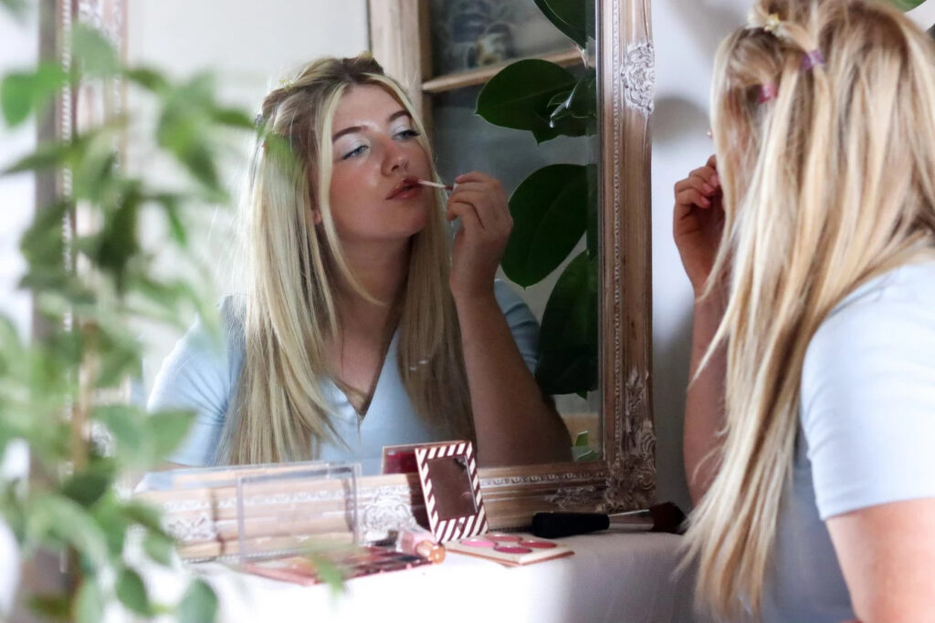 Nina Collins putting on makeup in front of a mirror
