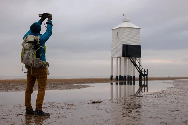 Photographer taking a picture of a mini tower on the beach during low tide
