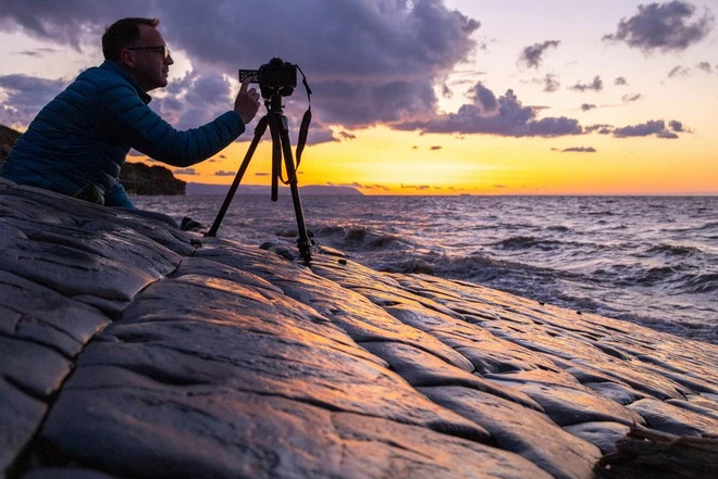 photographer taking a picture of the sunset next to the sea