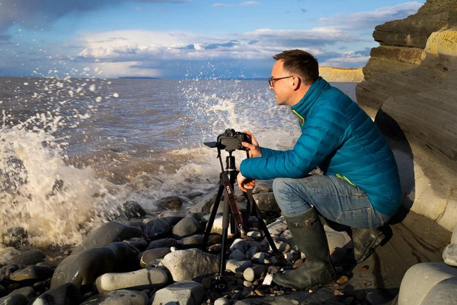 photographer taking photos on a beach as waves splash on the rocks
