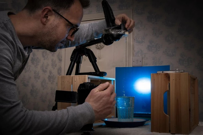 man taking a closeup photo of water drops dripping into a cup of water